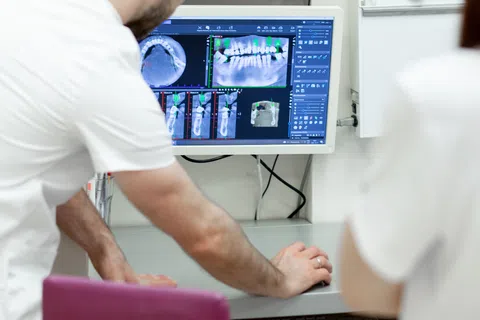 Dentist reviewing dental X-ray images on a computer screen during patient consultation in clinic.