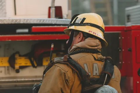 Firefighter in full gear with oxygen tank stands beside fire truck, preparing for emergency response.