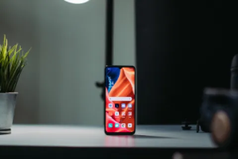 Smartphone with colorful screen standing on desk near plant and lamp in modern indoor setting
