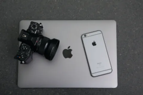 Black camera and silver iPhone on top of a closed MacBook laptop on a dark surface