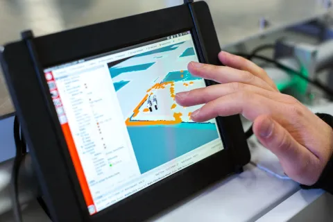Hand interacting with touchscreen tablet displaying 3D mapping and robotic navigation software interface.