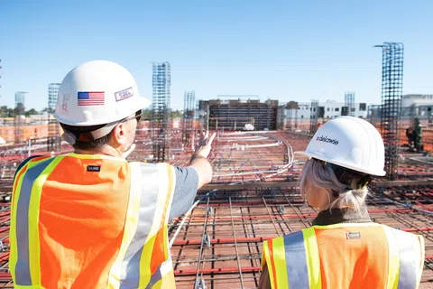 Construction workers in safety gear inspecting steel rebar framework at a large building site under clear sky.