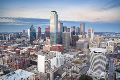Aerial view of Dallas downtown skyline with tall skyscrapers and city streets at dusk under a partly cloudy sky