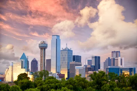 Dallas city skyline at sunset with high-rise buildings and vibrant colorful clouds above.