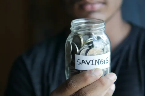 Person holding a clear jar filled with coins labeled savings focused on financial planning and money management.
