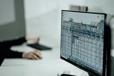 Person working on a computer with a 3D architectural design model in a program like AutoCAD displayed on the monitor screen.