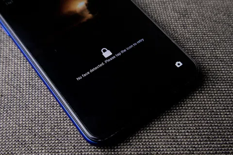 Smartphone screen shows no face detected message with lock icon on textured grey surface.