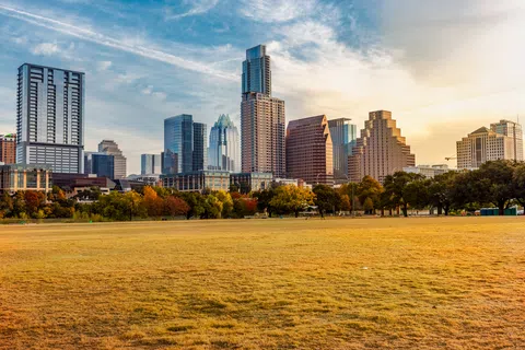 Austin city skyline with modern skyscrapers and autumn trees under a partly cloudy sky at sunset.