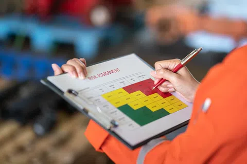 Person in orange safety gear marking a risk assessment matrix with red, yellow, and green zones on clipboard.