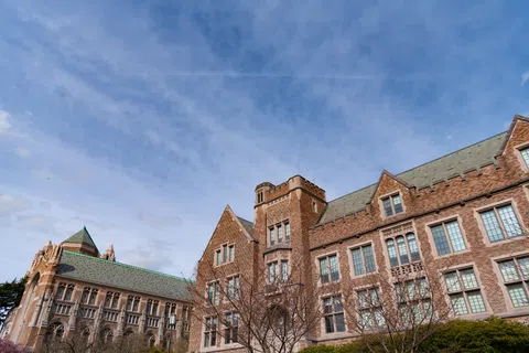 Historic university buildings with Gothic architecture under a partly cloudy blue sky.