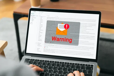Laptop screen showing email inbox with a large warning alert overlay and a red exclamation mark on envelope icon.