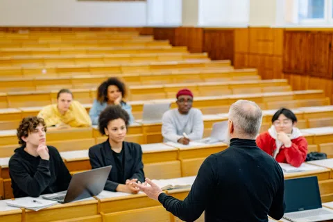 Professor teaching a small, diverse group of attentive students in a spacious university lecture hall.