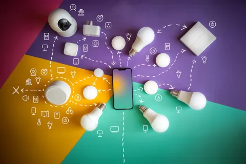 Smart home devices and light bulbs connected to a smartphone on a colorful background with tech icons.