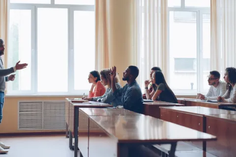 Teacher engaging diverse students in a classroom discussion with one student raising hand to answer a question