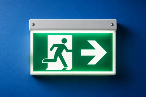 Illuminated green emergency exit sign with running figure pointing right on blue wall background