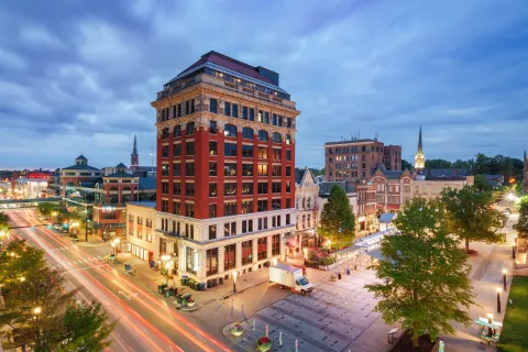 Historic red brick building in downtown city at dusk with busy light trails and surrounding architecture.