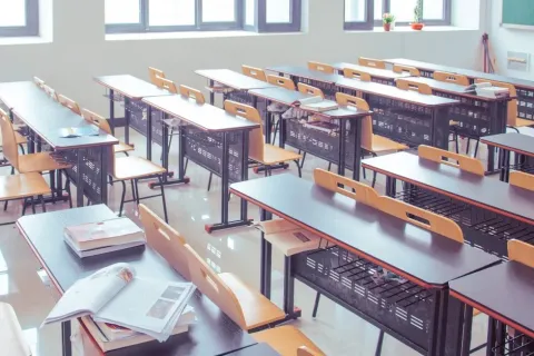 An empty classroom filled with desks. One desk has a various books on it.