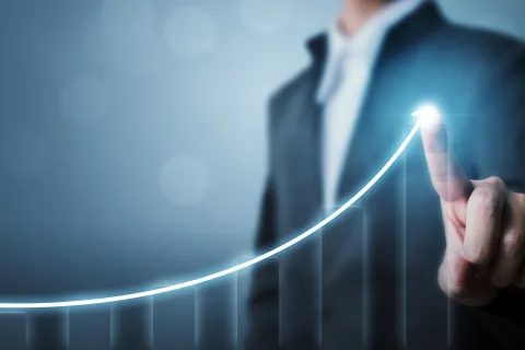 Businessman in suit pointing at ascending glowing graph line representing growth and success
