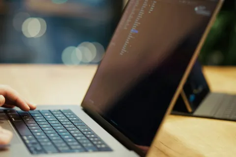 Person typing on laptop keyboard with code visible on screen in a focused workspace setting.