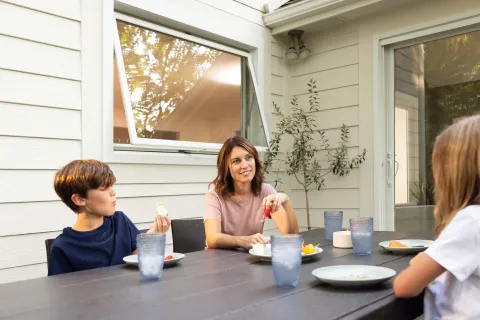 Family enjoying outdoor meal and conversation at backyard patio table with food and drinks on a sunny day