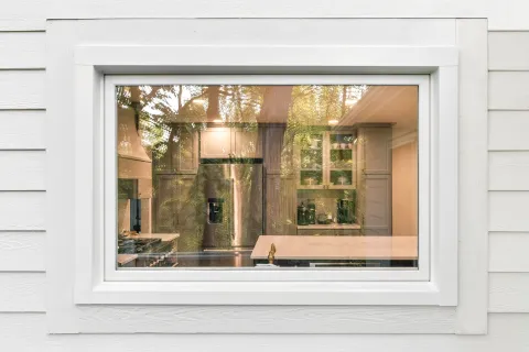 Modern kitchen with stainless steel refrigerator and cabinets seen through a white framed window