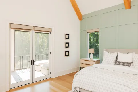 Bright modern bedroom with wooden floor, light green accent wall, large bed, and glass doors to balcony.