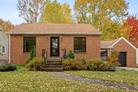 Charming red brick house surrounded by autumn foliage and a manicured lawn.