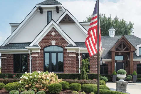 Elegant brick house with manicured garden, American flag, and clear blue sky.
