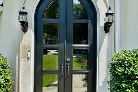 Elegant black double doors with arched design, flanked by lanterns and surrounded by lush greenery.