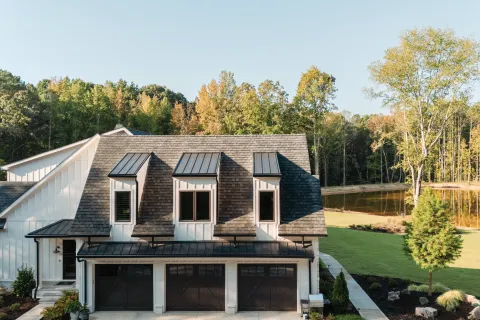 Modern farmhouse with triple garage and black trim surrounded by green lawn and trees under clear sky