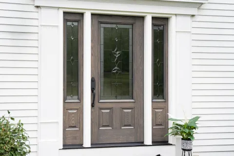 Elegant wooden front door with decorative glass panels and white exterior siding with potted plants.