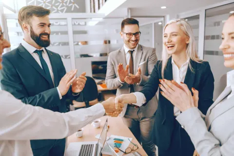 Business professionals shaking hands and celebrating successful deal in modern office meeting room.