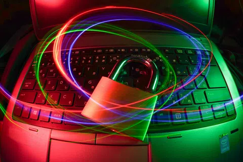 Metal padlock on laptop keyboard with swirling red, blue, and green light trails symbolizing cybersecurity and data protection.