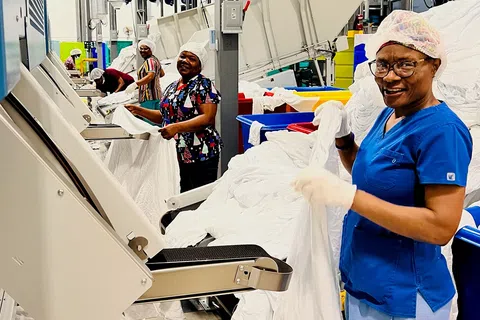 Workers in hairnets and gloves processing white linens using industrial machines in a textile factory.