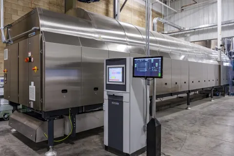 Large stainless steel industrial food processing machine with control panel in a clean factory setting