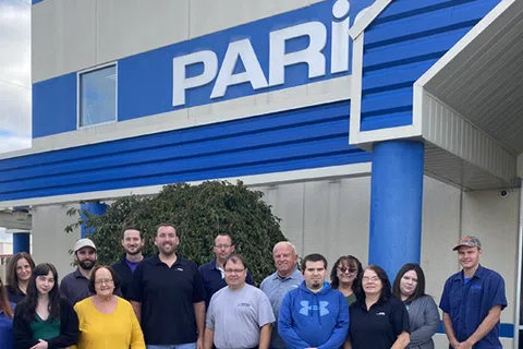 Group of employees standing outside a building with PARI sign and blue accents under a cloudy sky