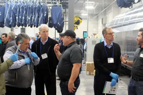 Group of men discussing and examining equipment in an industrial factory setting with hanging garments.