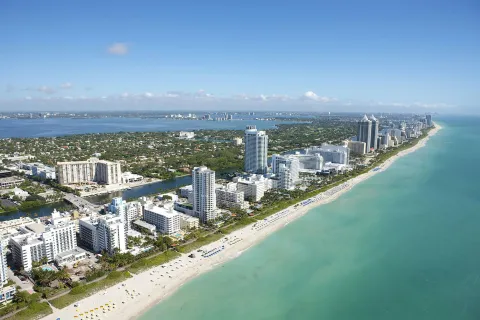 Aerial view of Miami Beach coastline with turquoise ocean, sandy beach, and high-rise buildings under clear blue sky.