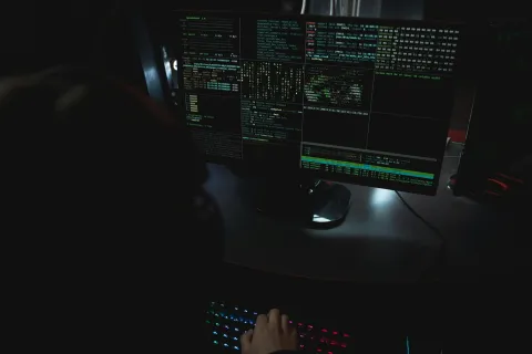 Person working on a computer with multiple coding and data analysis screens in a dark room.