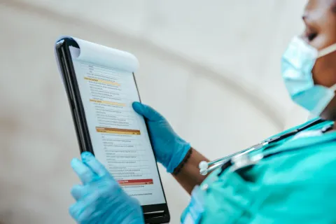 Healthcare professional in surgical gloves and mask reviewing medical checklist on clipboard.