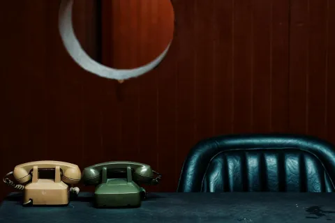 Retro beige and green rotary phones on a dark table with a blue leather chair and brown wooden wall background.