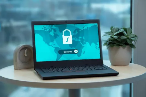 Laptop on round table showing secured network screen with lock icon and world map background.
