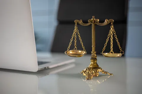 Golden balance scale on a desk next to a silver laptop, symbolizing justice and legal work in an office setting.