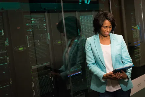 Woman in blue blazer using tablet in data center with server racks and reflections on glass wall