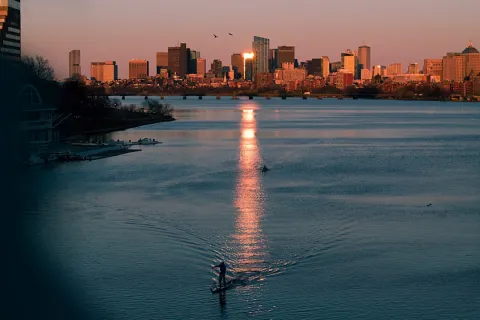 Paddleboarder on calm river at sunset with city skyline and golden light reflecting on water.
