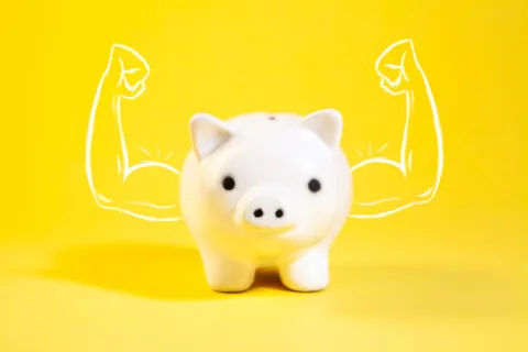 White piggy bank with drawn muscular arms on yellow background symbolizing strong savings.
