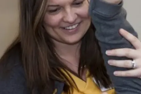 Smiling woman assists child with a physical therapy exercise in a bright indoor setting