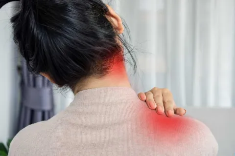 Woman with black hair holding her neck and shoulder showing redness indicating pain or discomfort.
