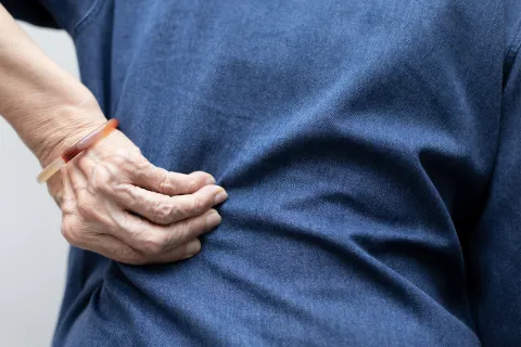 Elderly person gripping their side in pain wearing a blue shirt and a wristband close-up.