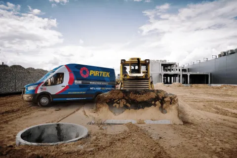 Pirtek service van and bulldozer at a construction site with dirt and concrete structure under cloudy sky